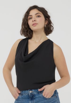 Top senza maniche nero con design a collo drappeggiato, realizzato in tessuto morbido. Indossato con jeans in denim blu a vita alta.