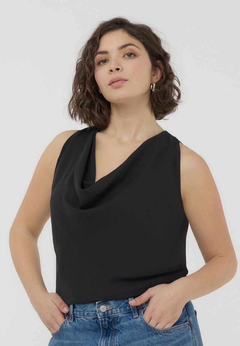 Top senza maniche nero con design a collo drappeggiato, realizzato in tessuto morbido. Indossato con jeans in denim blu a vita alta.