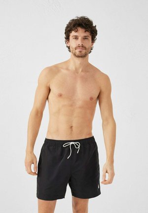 Bañador negro con cintura elástica y cordón blanco. Presenta un detalle de logo en la parte inferior izquierda.