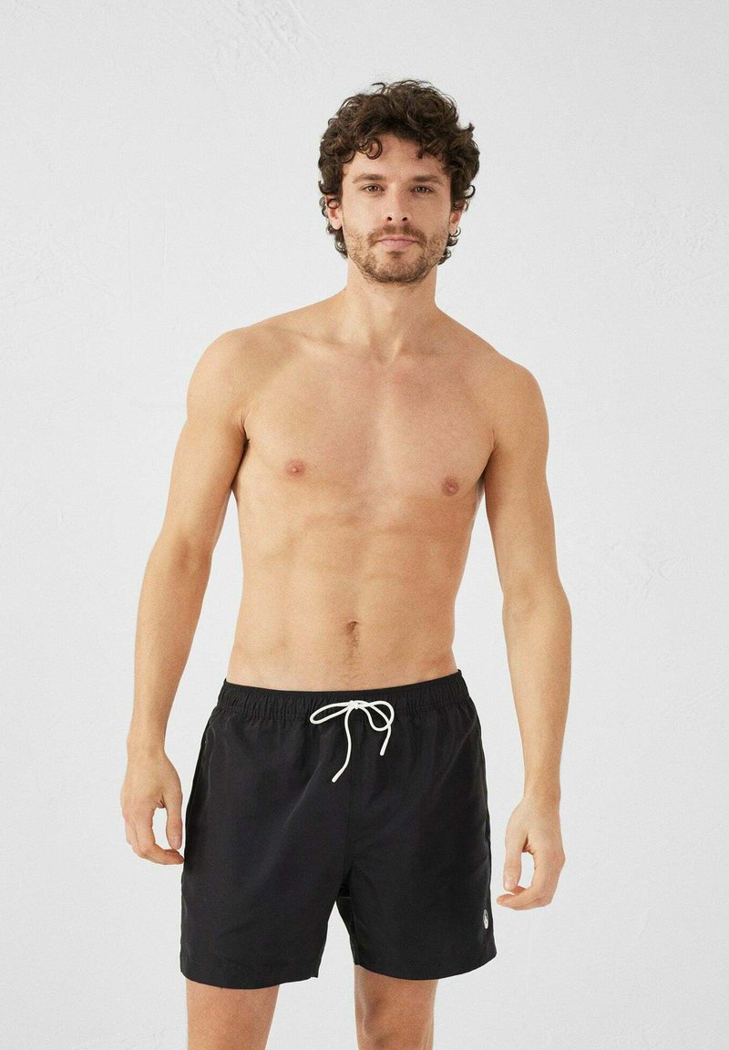 Shorts de bain noirs avec une taille élastique et un cordon de serrage blanc. Présente un accent logo sur le côté inférieur gauche.