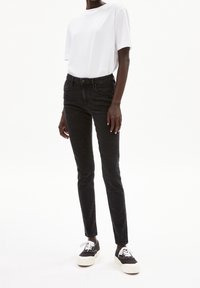 Jean skinny noir en denim associé à un t-shirt blanc uni et des baskets noires avec une semelle épaisse blanche. Design minimaliste.