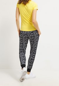 Zwarte gevoerde sweatpants met witte geometrische ontwerpen, geribbelde boorden, gecombineerd met een geel T-shirt met korte mouwen en witte sneakers.