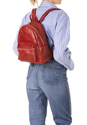 Persona che indossa uno zainetto rosso in pelle con tasche con cerniera, jeans blu e una maglia a maniche lunghe a righe blu e bianche.