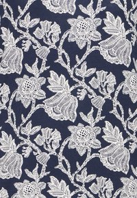 Motif complexe de vignes florales blanches et feuillues sur un fond de tissu bleu foncé, présentant des fleurs détaillées et des tiges enroulées.