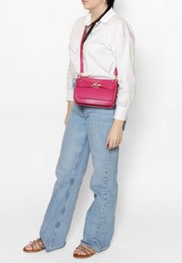 Borsa a tracolla in pelle fucsia con una superficie liscia, un pattino frontale con una chiusura in oro e una lunga tracolla regolabile. Forma rettangolare strutturata.