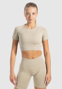 Beige sportoutfit bestaande uit een aansluitende crop top met korte mouwen en hoge taille shorts. Glad textuur met geribbeld taillebanddetail.