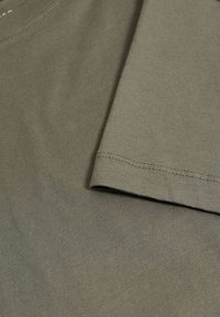 Olive zelené bavlněné tričko s kulatým výstřihem a krátkými rukávy. Hladká textura, viditelné detaily švů a ohrnovací rukávy.