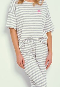Zestaw do relaksu w paski, składający się z luźnej, szaro-białej bluzki w paski z różowym serduszkiem oraz dopasowanych spodni ze ściągaczem. Miękka tekstura materiału.