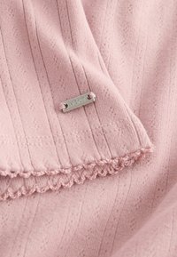 Tessuto di un delicato rosa con texture a righe verticali, caratterizzato da un bordo scallop e un piccolo etichetta metallica incisa con "NEXT". Aspetto morbido e liscio.