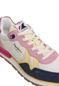 Sneaker, mille valge nahk, roosa ja kollane nubuck-accents, tekstureeritud tumesinised osad ja koorevärvi paelad. Omab logo silti keele peal.