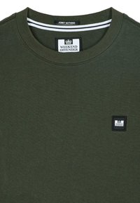 Camiseta de cuello redondo en verde oscuro con parche del logo "Weekend Offender" en el pecho y etiqueta "Admit Nothing" en el interior del cuello.