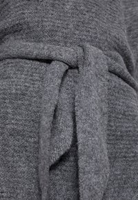 Nahaufnahme eines grauen gestrickten Stoffgürtels, der in einem Knoten um ein passendes strukturiertes Kleidungsstück gebunden ist.