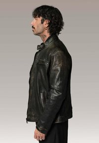 Veste en cuir noir avec une finition légèrement usée, poches zippées, col montant et silhouette ajustée. Détails de surface texturée.