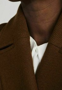 Brown textured coat collar with a white shirt underneath. Features a tailored design and visible stitching along edges.