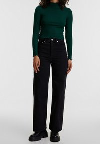 Green ribbed long-sleeve top with a mock neck, paired with high-waisted black wide-leg jeans and chunky black platform boots.