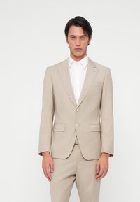 Világos bézs, szabott öltöny, amelyen bemetszett gallér, két gombos záródás és oldalsó zsebek találhatók. Fehér, gombos ing fölött viselik.