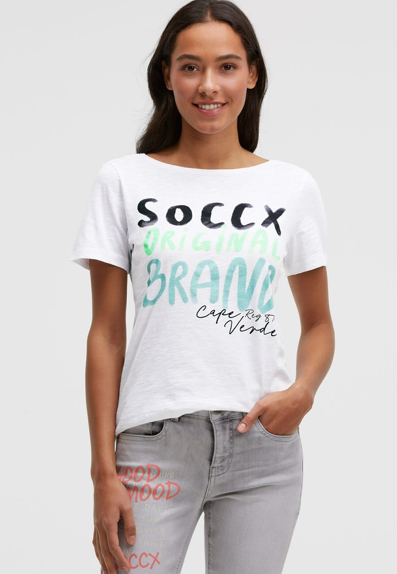 Weißes T-Shirt mit kurzen Ärmeln und mehrfarbigem Text: "SOCCX ORIGINAL BRAND" und "Kap Verde." Kombiniert mit hellgrauen Jeans mit Print-Details.