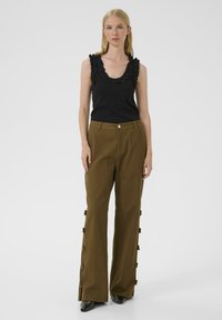 Black tank top with ruffled neckline paired with olive green wide-leg trousers featuring button closure and side bows. Smooth fabric texture.