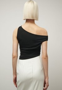 Mustat yhden olkapään paita pehmeää puuvillaa, jossa on rypytetty rakenne takana, yhdistetty valkoisiin raidallisiin hameeseen.