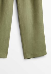 Gros plan sur un pantalon en lin vert olive montrant des jambes droites larges et une texture de tissu lisse sur un fond blanc.