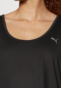 Top sportivo nero senza maniche con scollatura rotonda e logo grigio Puma sul lato sinistro del petto. Il tessuto sembra liscio e leggero.