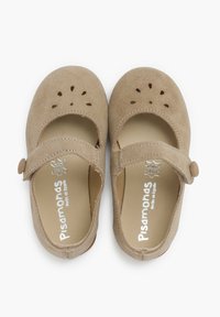 Jasnobrązowe zamszowe buty Mary Jane z dekoracyjnymi wycięciami, paskiem z guzikiem i miękką wyściółką wewnętrzną. Logo wydrukowane w srebrnym kolorze na wkładce.