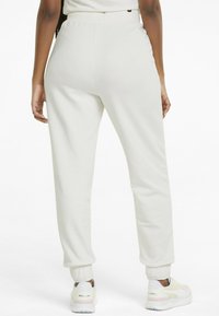 Pantaloni jogger grigi chiari con vita e polsini elasticizzati, caratterizzati da una texture liscia e una vestibilità rilassata, abbinati a sneakers bianche.