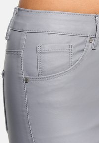 Grauer Kunstlederrock mit dekorativen Nähten, seitlichen Taschen und metallic Nieten. Die glatte Textur und das figurbetonte Design betonen die Kurven.