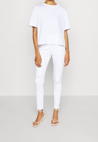 Camiseta de algodón blanca de manga corta y corte holgado, combinada con jeans blancos ajustados con roturas en las rodillas y tacones blancos atados.