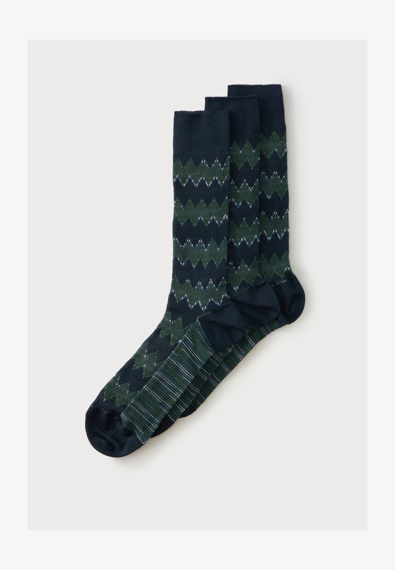 Trois paires de chaussettes bleu foncé avec des motifs en zigzag verts et blancs et rayés, disposées côte à côte sur un fond blanc.