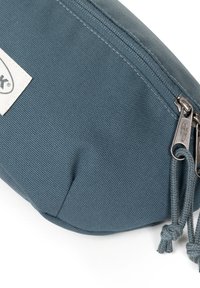 Astuccio per matite in tessuto blu con finitura testurizzata, dotato di chiusura a zip, elementi in metallo e una etichetta con scritta sul lato.