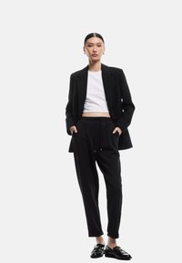 Sort skræddersyet blazer over en hvid cropped skjorte, parret med sorte snørespants og skinnende sorte sko. Minimalistisk design og glat tekstur.