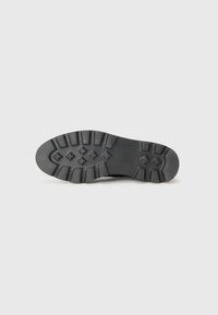 Semelle de chaussure en caoutchouc noir avec un motif texturé, présentant des rainures et des crêtes prononcées pour une meilleure adhérence. Durable et conçue pour la traction.