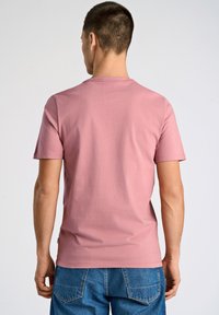 T-shirt med kort ärm, rund halsringning i ljusrosa bomull, med en avslappnad passform och enkel design, kombinerad med blå denimbyxor.