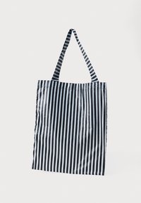 Stripet totebag med svarte og hvite vertikale striper, laget av et glatt, blankt materiale, med to korte håndtak for bæring.