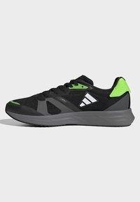 Scarpe da ginnastica nere con accenti verdi, parte superiore in mesh e suola testurizzata. Presentano un logo prominente e un'intersuola imbottita per il supporto.