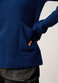 Pull en maille côtelée bleu marine avec une finition texturée, comportant une poche avant et des manches longues. Assorti à un jean en denim foncé.