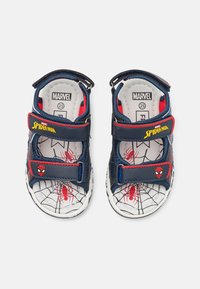 Laivastonsinisiä sandaaleja, joissa on punaisia ja mustia korostuksia, sisältäen Spider-Man-kuvioiset pohjalliset ja velcro-hihnat turvalliseen istuvuuteen. Säädettävä kantapää- ja varvaspeitto.