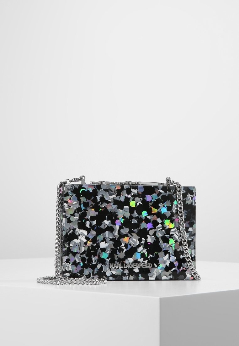 Borsa rettangolare nera con design di coriandoli metallici multicolori, tracolla in catena argento e dettaglio del logo sulla parte anteriore. Texture liscia.