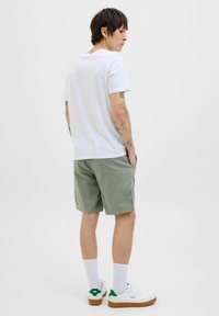 Camiseta blanca de algodón, pantalones cortos verde oliva, zapatillas blancas con acentos verdes y calcetines blancos. Diseño casual y relajado con bolsillos.