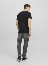 Black short-sleeve t-shirt paired with gray denim jeans, featuring a slim fit and rolled cuffs, complemented by black high-top sneakers.