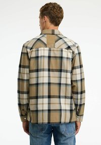 Camisa de cuadros en tonos beige, marrón y negro, con material de franela, mangas largas, puños abotonados y un detalle de canesú en la parte posterior.