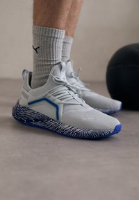 Light gray athletic shoes with blue accents, textured upper, and patterned sole. Socks are ribbed gray. Black ball in the background.