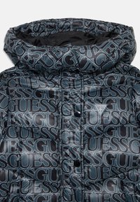 Pufferjakke med et glansfullt svart og grått gjentakende "GUESS"-logo mønster, med høy krage og knappelukking foran.