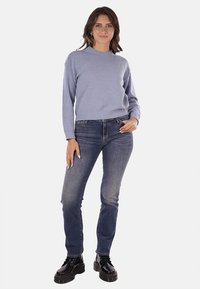 Maglione azzurro chiaro a maglia con scollatura rotonda, abbinato a jeans blu scuro e stivali neri con lacci. Texture liscia con polsini a costine.