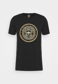 Černé tričko s krátkým rukávem a kulatým zlatým grafickým designem s emblémem a textem "GLORIOUS GANGSTA" ve zlatém písmu.