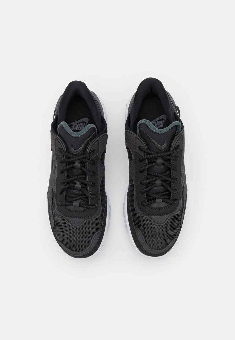 Zapatillas negras con parte superior de malla, superposiciones texturizadas y detalles en gris. Presentan un diseño de cordones y una suela blanca de goma.