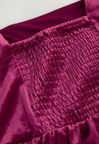 Rochie de catifea fucsia cu un corset elastic, detaliu texturat și tiv inferior rugos. Material moale cu un luciu strălucitor.