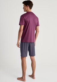Kurzärmliges bordeauxrotes T-Shirt, kombiniert mit gemusterten marineblauen Shorts, die weiße geometrische Designs aufweisen, aus glattem Stoff sind und einen entspannten Schnitt haben.