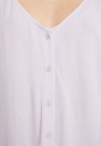 Light lavender blouse featuring a textured fabric, V-neckline, and six matching buttons down the front. Soft, breathable material.